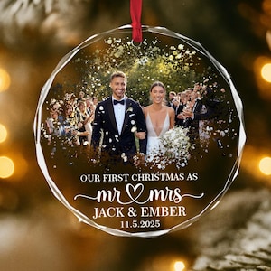 May include: A clear, faceted glass Christmas ornament with a wedding photo inside. The ornament has a red ribbon for hanging and features the text "OUR FIRST CHRISTMAS AS mr & mrs JACK & EMBER 11.5.2025".