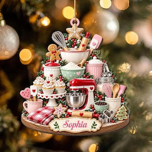 May include: A Christmas tree-shaped ornament featuring miniature baking supplies including a red stand mixer, mixing bowls, a gingerbread man, cupcakes, and kitchen utensils. A plaque at the base displays the name Sophia in pink script.