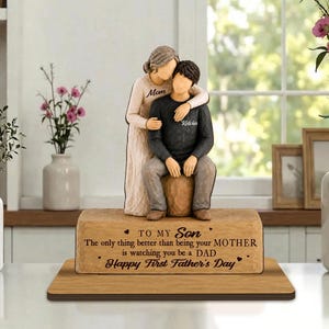 May include: A decorative figurine of a mother standing behind her son who is sitting on a wooden block. The mother wears a long beige dress and the son wears a dark sweater and gray pants. The base features the text: TO MY SON The only thing better than being your MOTHER is watching you be a DAD Happy First Father's Day.