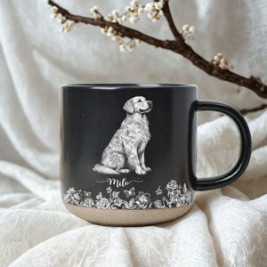 May include: Black ceramic mug featuring a detailed illustration of a Golden Retriever with floral accents. The mug has a black handle and a natural-colored base. The dog's name, "Milo," is written below the illustration.