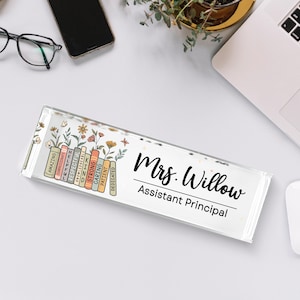 May include: A clear acrylic desk nameplate with the name "Mrs. Willow, Assistant Principal" in black script. The left side features a colorful design of books and flowers with positive adjectives.