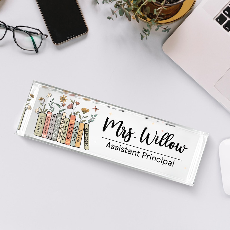 May include: A clear acrylic desk nameplate with the name "Mrs. Willow, Assistant Principal" in black script. The left side features a colorful design of books and flowers with positive adjectives.