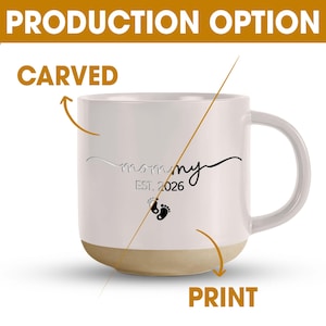 May include: White ceramic mug with a beige base and a white handle. The mug features the word "mommy" in a script font, the year "EST. 2026", and baby footprints. The mug is a production option, available carved or printed.