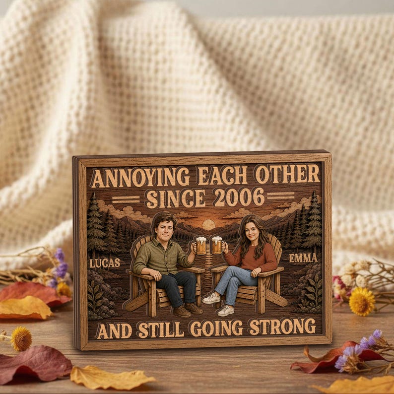 May include: A rectangular wooden sign featuring a printed illustration of two people sitting in chairs, holding beer mugs, with a mountain and forest background. The text reads: ANNOYING EACH OTHER SINCE 2006, LUCAS, EMMA, AND STILL GOING STRONG.