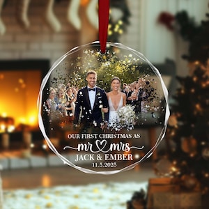May include: A clear, faceted Christmas bauble with a wedding photo inside. The photo shows a smiling couple walking with guests. Text reads "OUR FIRST CHRISTMAS AS mr & mrs JACK & EMBER 11.5.2025". A red ribbon is attached.