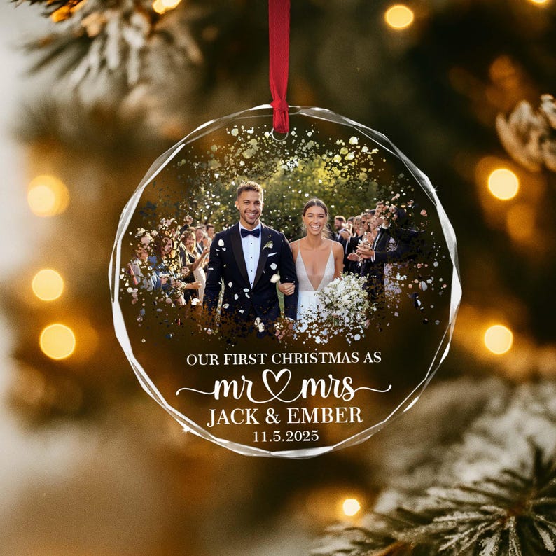 May include: A clear, faceted glass Christmas ornament with a wedding photo inside. The ornament has a red ribbon for hanging and features the text "OUR FIRST CHRISTMAS AS mr & mrs JACK & EMBER 11.5.2025".