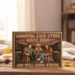 May include: A rectangular wooden sign featuring a laser-engraved illustration of two people sitting in chairs, holding beer mugs, with a mountain and forest background. The text reads: ANNOYING EACH OTHER SINCE 2006, LUCAS, EMMA, AND STILL GOING STRONG.