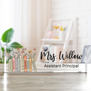 May include: A clear acrylic desk sign with the name "Mrs. Willow" and the title "Assistant Principal" in black script. The left side features a floral design with colorful books labeled with positive attributes.