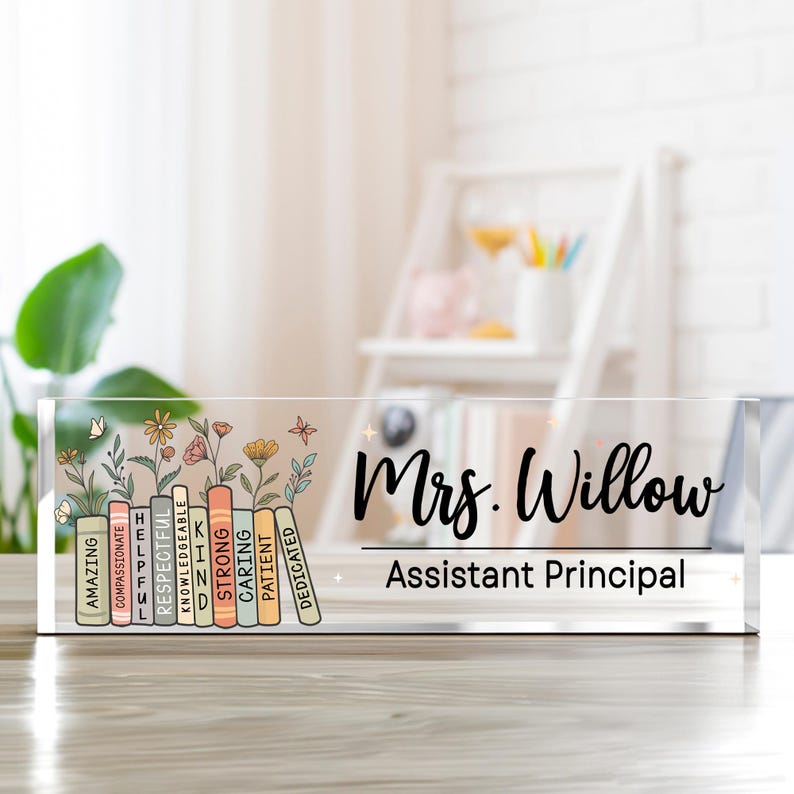 May include: A clear acrylic desk sign with the name "Mrs. Willow" and the title "Assistant Principal" in black script. The left side features a floral design with colorful books labeled with positive attributes.
