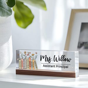 May include: A clear acrylic desk sign with a wooden base. The sign features the name "Mrs. Willow" and the title "Assistant Principal" in black script. Colorful books with positive words and floral accents are on the left.