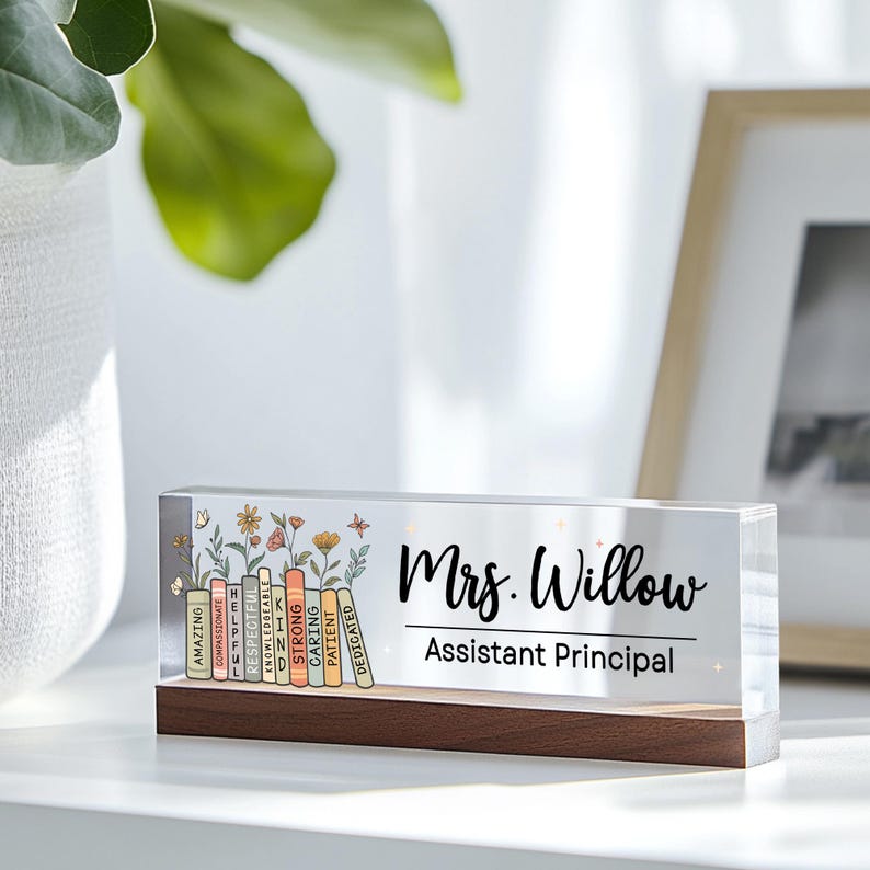 May include: A clear acrylic desk sign with a wooden base. The sign features the name "Mrs. Willow" and the title "Assistant Principal" in black script. Colorful books with positive words and floral accents are on the left.