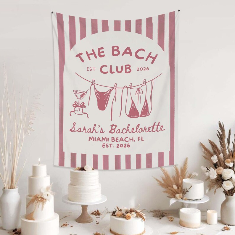 May include: A white and pink striped tapestry with the text "THE BACH CLUB EST 2026" and "Sarah's Bachelorette MIAMI BEACH, FL EST. 2026". The design includes a cocktail and lingerie hanging on a clothesline. The tapestry is displayed above several cakes.