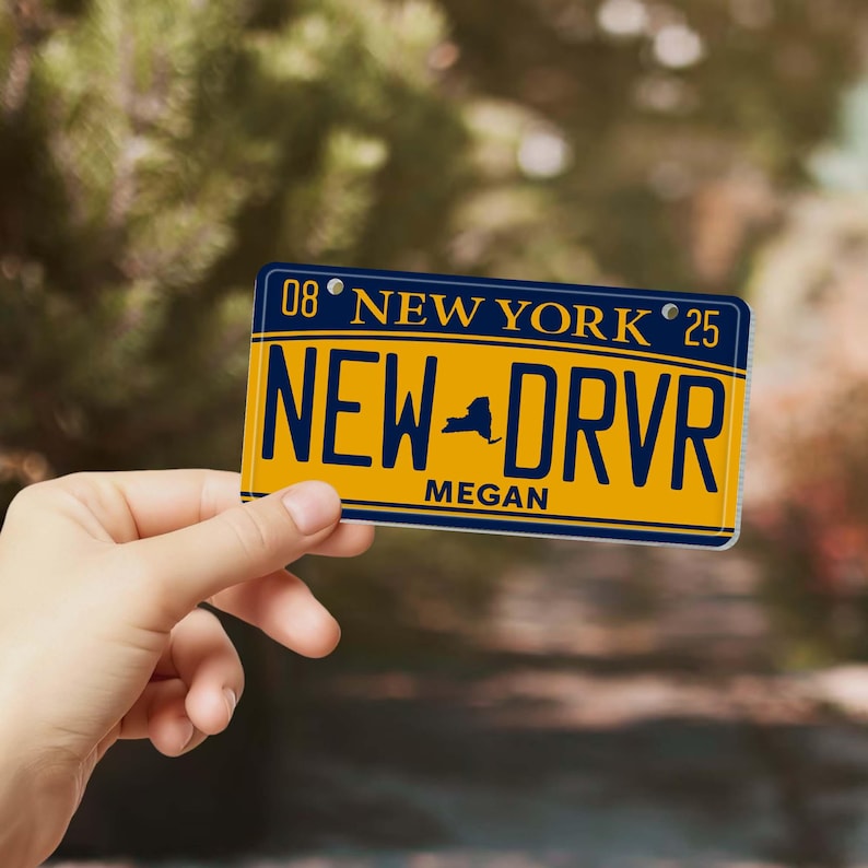 Puede incluir: Una placa de matr&iacute;cula amarilla y azul de Nueva York con el texto "NEW DRVR" y el nombre "Megan". La placa tambi&eacute;n tiene el texto "NEW YORK" y los n&uacute;meros "08" y "25".