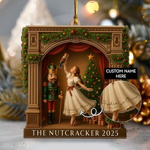 May include: Wooden Christmas ornament featuring a scene from The Nutcracker ballet. The ornament depicts a ballerina, a nutcracker soldier, and a Christmas tree. The text "THE NUTCRACKER 2025" is at the bottom. The ornament has a gold string for hanging.