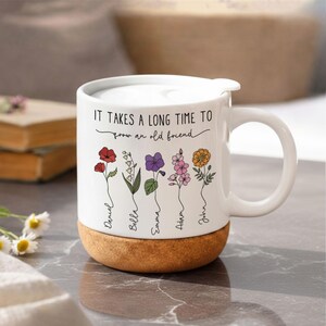 May include: White ceramic mug with a cork base and a white lid. The mug features a floral design with the text "IT TAKES A LONG TIME TO grow an old friend" and names below the flowers. The mug has a handle.