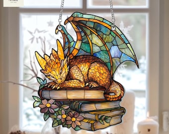 Peut inclure: Une suspension en verre coloré représentant un dragon doré aux ailes bleues et vertes reposant sur une pile de livres. Le dragon a une expression féroce et est entouré de fleurs.