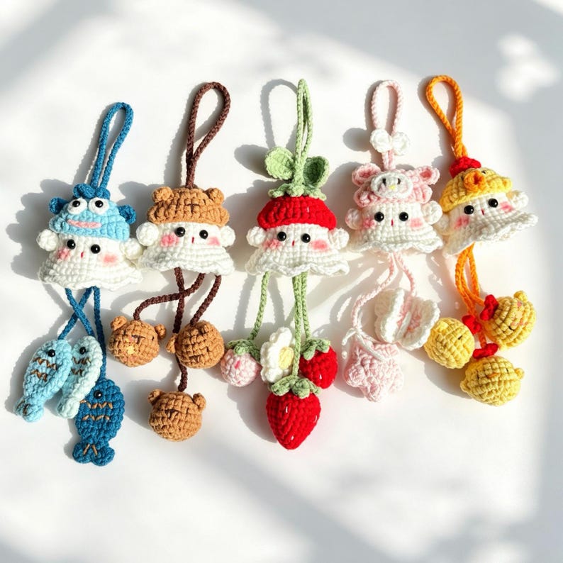 K&ouml;nnte beinhalten: F&uuml;nf handgefertigte H&auml;kelanh&auml;nger mit kleinen Figuren mit H&uuml;ten und baumelnden Elementen. Die Anh&auml;nger umfassen ein blaues Fischmotiv, ein braunes B&auml;renmotiv, ein rotes Erdbeermotiv, ein rosa Blumenmotiv und ein gelbes K&uuml;kenmotiv, alle mit Schlaufen.