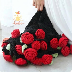 May include: A black crocheted bag adorned with vibrant red roses and green leaves. The bag is held by a person, showcasing the handmade floral design. The logo "koko" is visible in the upper left corner.