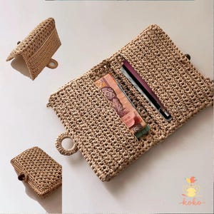 Op de afbeelding: Een beige gehaakte clutch met een houten knoopsluiting, open getoond met geld en een pen erin. Een kleinere bijpassende clutch is ook afgebeeld. De clutch heeft een ronde handgreep en een getextureerde, geweven uitstraling.