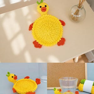 May include: A handmade yellow crochet duck coaster with orange feet and beak, and green accents. The duck-shaped coaster is designed to hold a glass or cup. The coaster is on a light-colored surface.