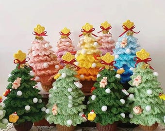 May include: A collection of colorful, crocheted Christmas trees. Each tree is a different color, including green, pink, yellow, and blue. They are decorated with white pom-poms, small ornaments, and topped with a yellow star and red ribbon. The trees sit on wooden bases.