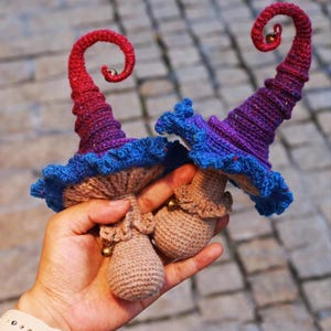 May include: Two handmade crochet mushroom hats with curled tips. The hats feature a color gradient from red to purple, blue frills, and a tan mushroom cap. Each hat has a small gold bell at the tip and base.