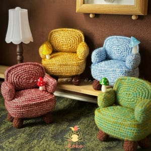 Può includere: Quattro poltroncine all'uncinetto in miniatura nei toni del rosso, giallo, blu e verde. Ogni sedia ha un accento a forma di fungo e gambe marroni. Le sedie sono disposte su una mensola con una lampada e un quadro sullo sfondo. La parola "koko" è visibile.