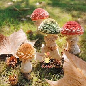 May include: A collection of handmade crochet mushrooms in various colors, including red, orange, and green, with white polka dots on the caps. The mushrooms are arranged on a bed of grass and fallen leaves, with a logo that says "koko".
