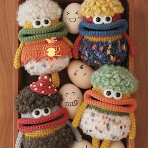 May include: A collection of handmade crochet dolls with whimsical features, including large eyes, colorful outfits, and fluffy hair. The dolls are arranged with eggs that have drawn faces, creating a playful scene.