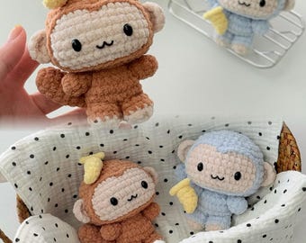 May include: Crocheted monkey toys in shades of brown and blue, each holding a yellow banana. The monkeys have black eyes and a smiling mouth. One monkey is held by a hand, while others are in a basket.