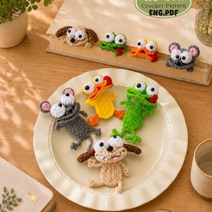 May include: A collection of small, crocheted animal figures including a gray mouse, a yellow duck, a green frog, and a tan dog, all featuring large white eyes with black pupils. A label reads NO-Sew Crochet Pattern ENG.PDF.