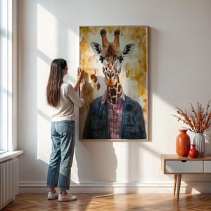 May include: A framed art print featuring a giraffe wearing a plaid shirt and denim jacket. The giraffe's portrait is set against a textured, abstract background with warm tones. The artwork is displayed on a white wall.