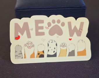 May include: A white sticker with the word "MEOW" in pink letters and a paw print in the middle. The sticker has a border of small pink hearts and seven paw prints in a row at the bottom.
