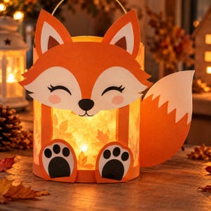 May include: A cylindrical lantern featuring a fox face design with orange and white paper cutouts, closed eyes, and pink cheeks. The body is illuminated from within, displaying a translucent leaf pattern, and includes a large orange fox tail.