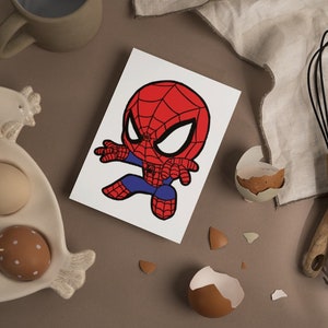 May include: A white card with a cartoon illustration of a red and blue Spiderman character with a black outline. The character is in a superhero pose with one arm outstretched and the other arm bent at the elbow.