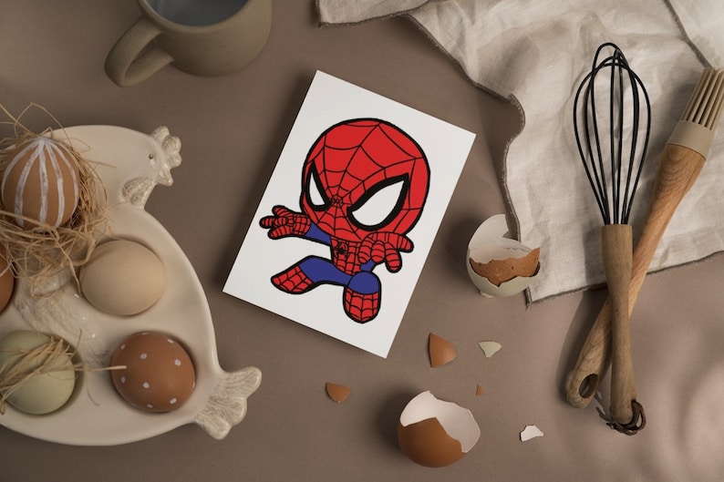 May include: A white card with a cartoon illustration of a red and blue Spiderman character with a black outline. The character is in a superhero pose with one arm outstretched and the other arm bent at the elbow.