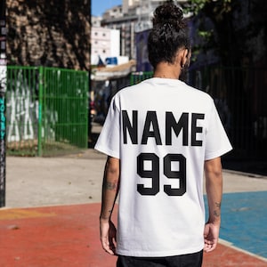 May include: White t-shirt with black text on the back that says "NAME 99".
