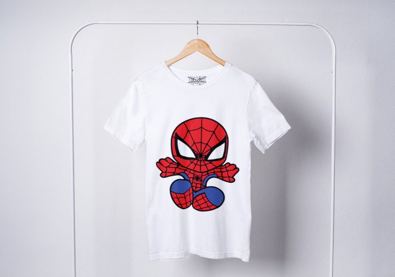 May include: White t-shirt with a cartoon image of Spiderman in a red and blue suit. The image shows Spiderman in a jumping pose with his arms outstretched.