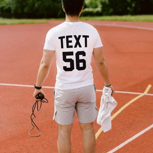 May include: A person wearing a white t-shirt with the text "TEXT 56" printed on the back. They are standing on a red track and holding a jump rope.