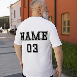 May include: White t-shirt with black text on the back that says "NAME 03".