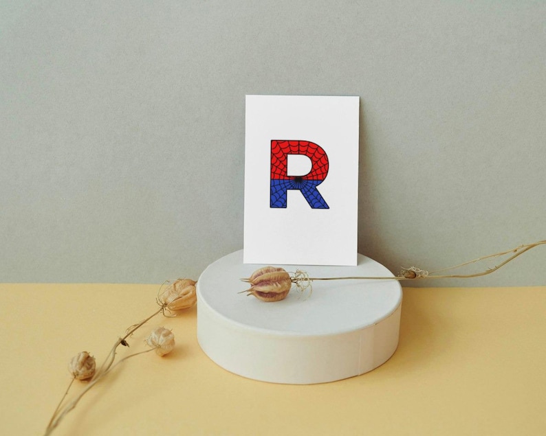 May include: A white card with a red and blue letter R on it. The letter R is filled with a pattern that resembles a spider web.