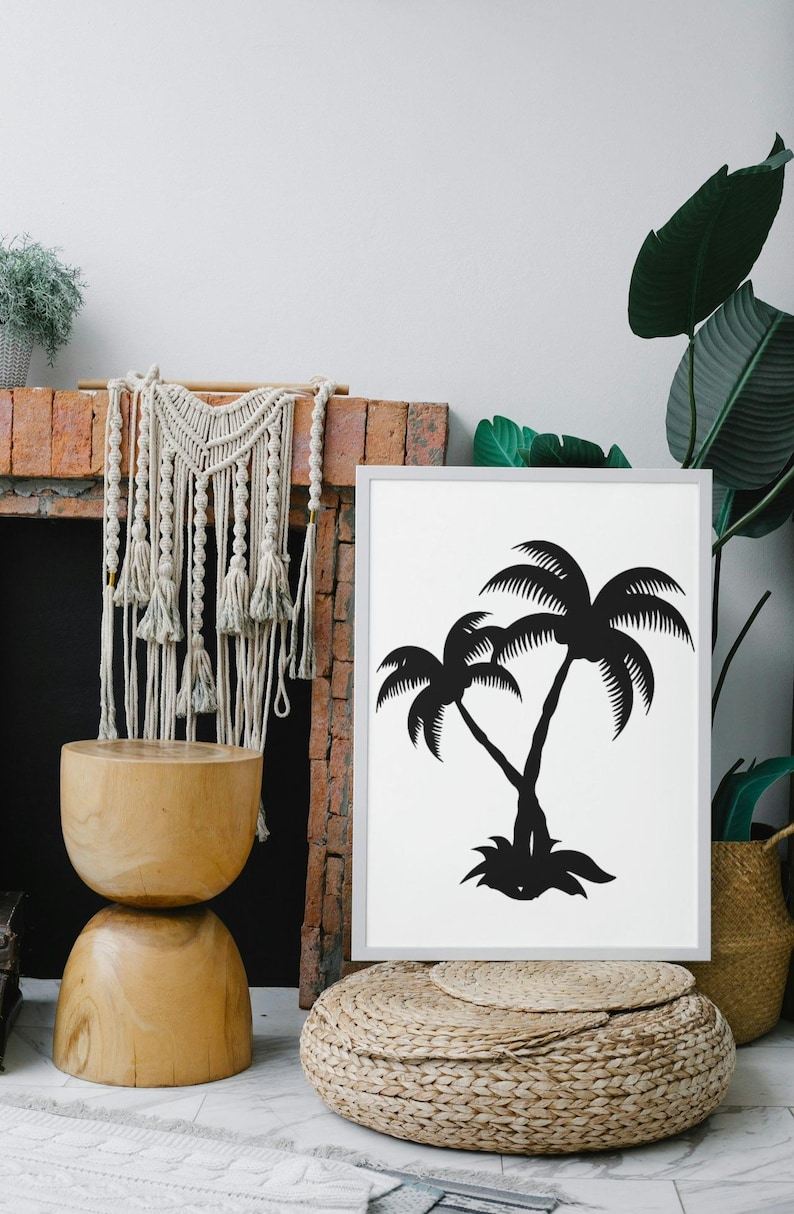 May include: A black and white print of two palm trees in a white frame. The print is hanging on a brick wall above a wooden stool and a woven ottoman.