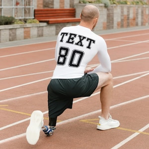 May include: A white long-sleeved shirt with black text that says "TEXT 80" on the back. The person is wearing black shorts and white athletic shoes. The person is on a red running track.
