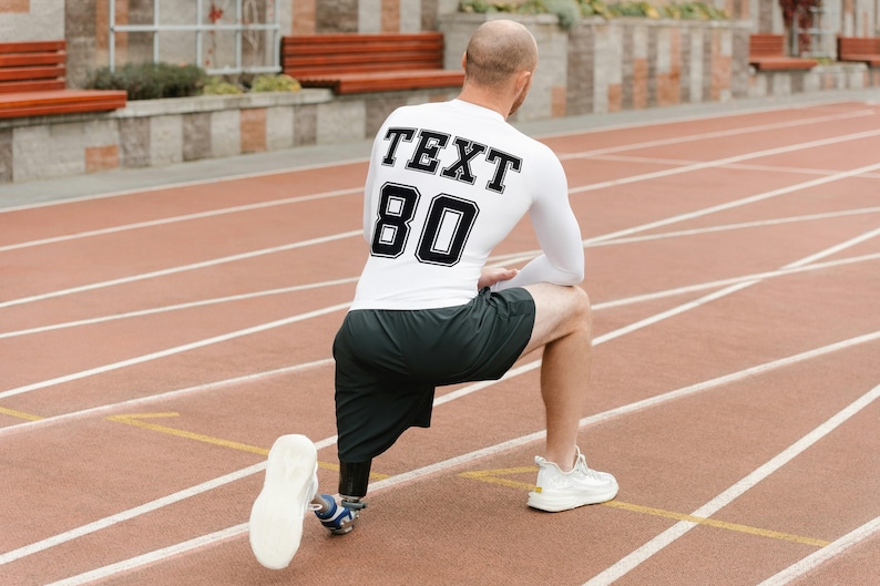 May include: A white long-sleeved shirt with black text that says "TEXT 80" on the back. The person is wearing black shorts and white athletic shoes. The person is on a red running track.