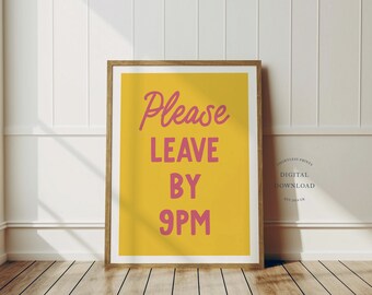 May include: A framed print with a yellow background and pink text that reads "Please LEAVE BY 9PM." The print is in a wooden frame and is displayed against a white wall and wooden floor.