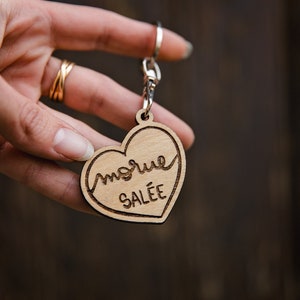 May include: A wooden heart-shaped keyring with the text "morue salée" engraved on it. The keyring is attached to a silver metal ring.