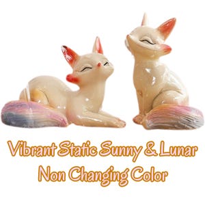 Puede incluir: Dos figuras de zorro de color crema con puntas de orejas naranjas y colas multicolores. Un zorro est&aacute; acostado mientras el otro est&aacute; sentado. El texto debajo dice: Vibrant Static Sunny & Lunar Non Changing Color.