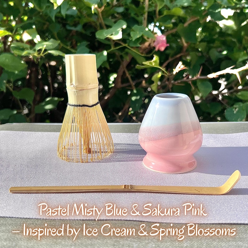 May include: A bamboo matcha whisk, a ceramic whisk holder with a white top and pink base, and a long bamboo scoop. The text reads: Pastel Misty Blue & Sakura Pink &ndash; Inspired by Ice Cream & Spring Blossoms. The items are arranged on a light surface.