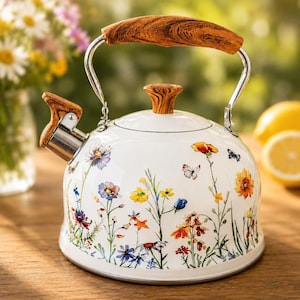 May include: A white tea kettle featuring a colorful floral pattern with various wildflowers and small butterflies. The kettle has a curved handle and a lid knob both finished in a wood grain pattern, along with a stainless steel spout and trim.