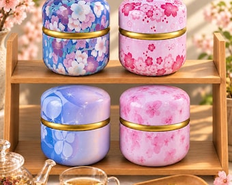 May include: Four round metal tea canisters with lids, arranged on a two-tier wooden shelf. Two canisters feature purple and blue floral patterns, while the other two display pink cherry blossom designs. Each container has a gold-colored band.